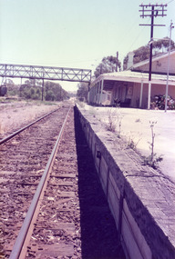 Looking along railway tracks to the railway station. There is a walkover bridge in the distance.