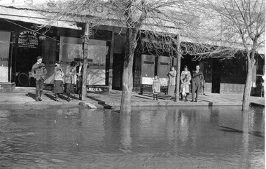 Flood waters in the main street. People are standing in front of shops
