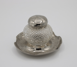 Glass inkwell with silver lid, standing on silver dish stand.