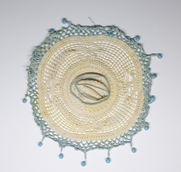 Circular lace and crochet milk jug cover with blue beads.