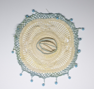 Circular lace and crochet milk jug cover with blue beads.