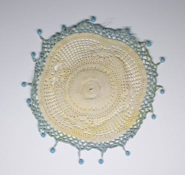 Circular lace and crochet milk jug cover with blue beads.