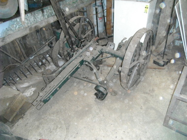 A horse-drawn sickle-bar mower with two wheels attached to a long bar with green edge.