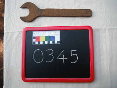 photograph of spanner, board, resting on white paper sheet