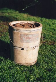 Medium wooden pail with heavy metal lid, used for making ice cream by stirring handle until contents thicken.