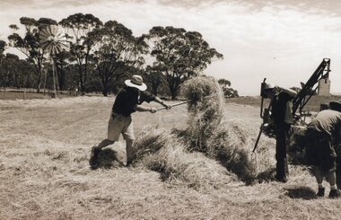 Photograph of men raking and gathering hay