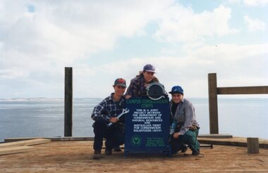 Photograph of people posing around a sign