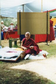 Photograph of Tibetan monk sitting in front of a trunk