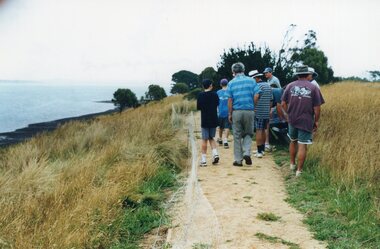 Photograph of people walking along a sand path