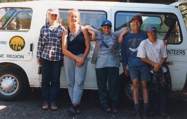 Photograph of five people posing in front of a minibus