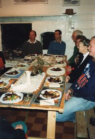 Photograph of people gathered around a table, eating.