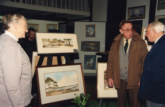 photograph of three people standing in front of paintings
