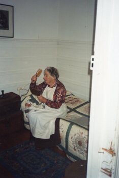 Colour photograph of woman sitting on bed