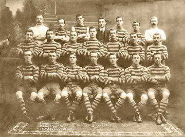 Photo shows 17 Players are wearing horizontal hoop long sleeve jumpers with matching socks, one is wearing short sleeves.  One gentleman is dressed in a suit and two are dressed in white.