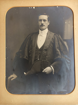 Formal portrait of a man in ceremonial robes holding a bicorn hat. His white shirt has a high collar and he is wearing a white bow tie.