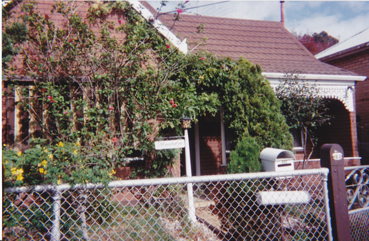 Front of a house including the garden and part of the fence and gate.