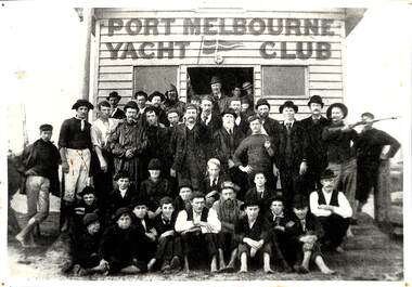 Black and white image of a group of men and boys posing outside a small wooden building identified as Port Melbourne Yacht Club.