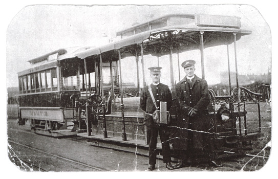 Two men in uniform stand in front of a cable tram looking at us.