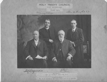 Four men, two seated and two standing behind them look towards the camera.