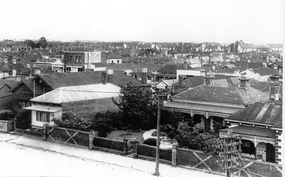 View from a raised position of a brick house set back from the road further than its neighbours giving it a larger front garden.