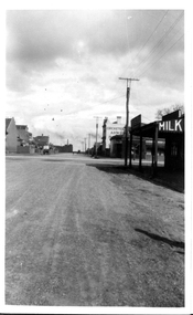 View looking along the street almost from ground level. The nearest visible building has a sign for "Milk" on the verandah. The words "Cricketers Arms" are mostly visible on the side of a building further along the street.