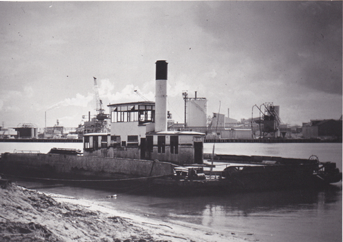 Black & white photo of a ferry docked on a river, industrial buildings in the background.