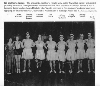 Photo shows seven Port Melbourne Football players dressed in white gathered skirts and bra tops, tiara's and jazz shoes.  Two women stand on the left end of a line, one is dressed in a long dark coloured dress and the other is in white shirt and shorts with straps. 