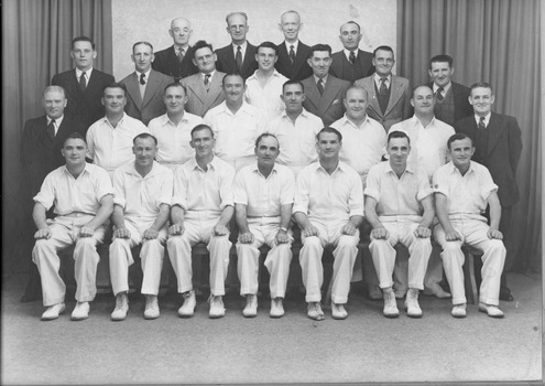 A group of twenty-six men pose in typical sporting club style in four rows. Fourteen men, mostly in the front two rows, are wearing cricket whites, the remaining men are wearing suits and ties.