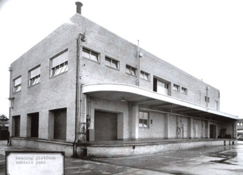 A substantial two storey brick building viewed at an angle with a loading dock along the longer side of the building.