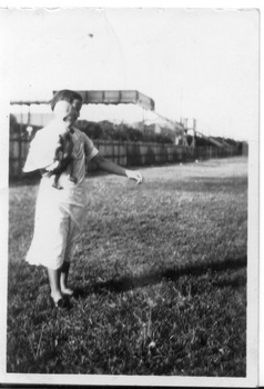 A woman stands side on to the camera with a toddler in her arms. There is a footbridge in the background.