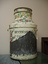The metal milk can that has been painted with coloured flowers on a cream background. A lot of the paint has peeled of but 'WOODRUF' and 'D A I' is still visible.