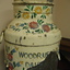 Closeup of the top half of a milk churn painted with colourful flowers on a cream background. The paint on the lower part of the churn is peeling badly but most of the name "Woodruff's Dairy" is still visible.