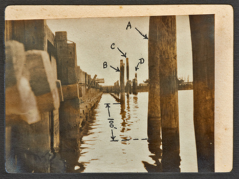 A low view of a pier or wharf, almost from water level, looking along the side of the structure with several freestanding pylons a short distance away in the water. Four of the pylons have been identified on the developed photograph as 'A', 'B', 'C' & 'D' and the distance between two of the pylons is identified as 100 feet. 