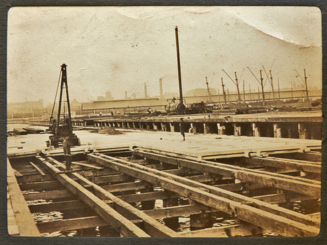A pier or wharf with some of the deck timbers removed or not yet installed with a man standing on the exposed beams.
