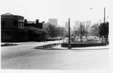 Intersection with garden in the middle and city buildings in the background.