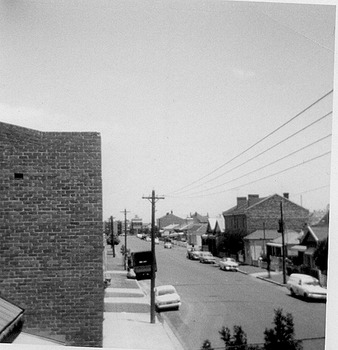 View of street contains housing and lined with cars on the roadside.