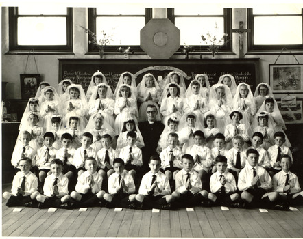 Black & white photo of children and a priest poising for their 1st communion photo.