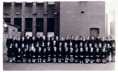 Black & white photo of children dressed I school uniform oping for their class photo.