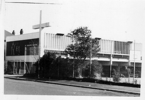 Black & white photo of a two storey building with a large cross in front of the building.