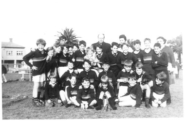 Boys football team posing informally with a priest and two women in the back row..