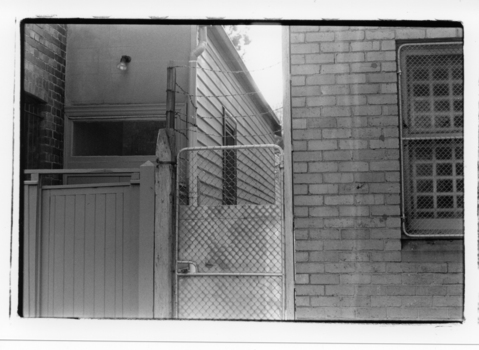 Image of brick building and weatherboard building,  with a timber & wired entrance gates.