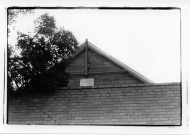 Black & white photo showing the roof valance and brick wall of a building.