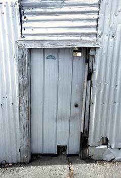 Metal gate set into a battered corrugated iron fence.