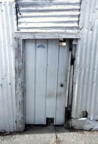 Metal gate set into a battered corrugated iron fence.