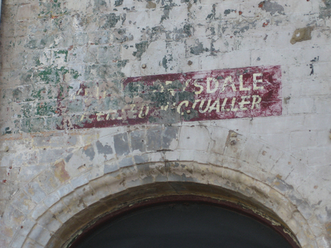 Old faded signage shown above an archway on an old building.
