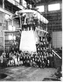 Black & white photo of workers gathered around machinery.