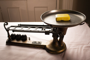 A set of manual scales with a bar of yellow soap sitting on the pan.