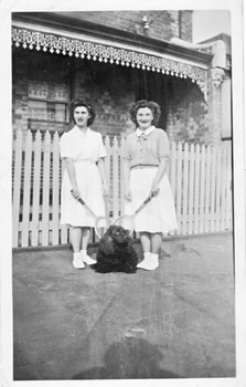 Two young women standing in a street with tennis rackets.