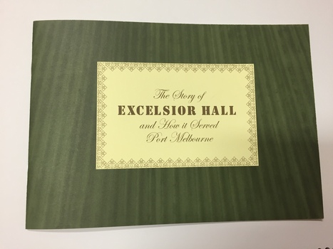 A rectangle shape green booklet with a yellow insert in the centre of the cover with the words The story of (in italics) Execelsior Hall (in a bold square font) followed by and how it served Port Melbourne (in italics) the wording is in a olive colour. 