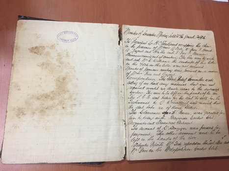 Image of an open old minutes book, 1936 - 1938.  One side shows water damage as well as the stamp of the club.  The other side shows hand written report.